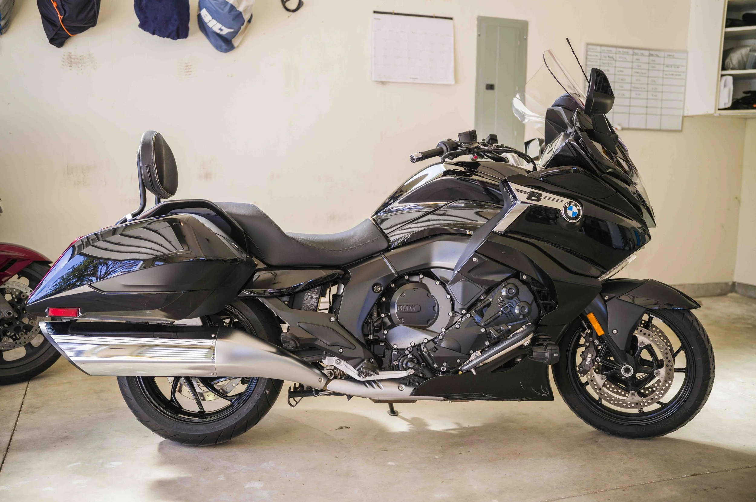 Black BMW motorcycle parked indoors, with a small backrest for the passenger, in a garage or storage area.