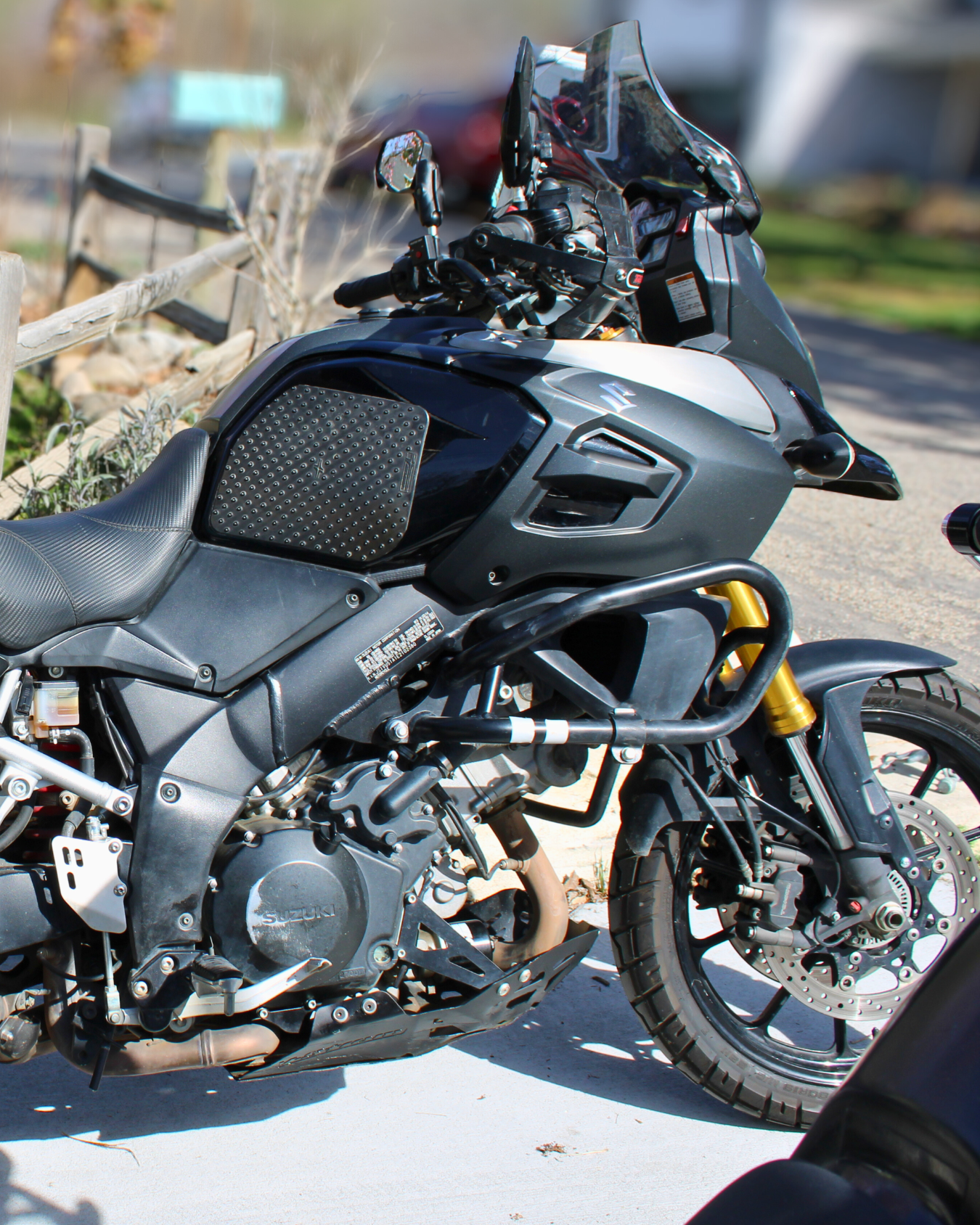 Black and gray Suzuki motorcycle parked outside on pavement with a black windscreen and gold front suspension.