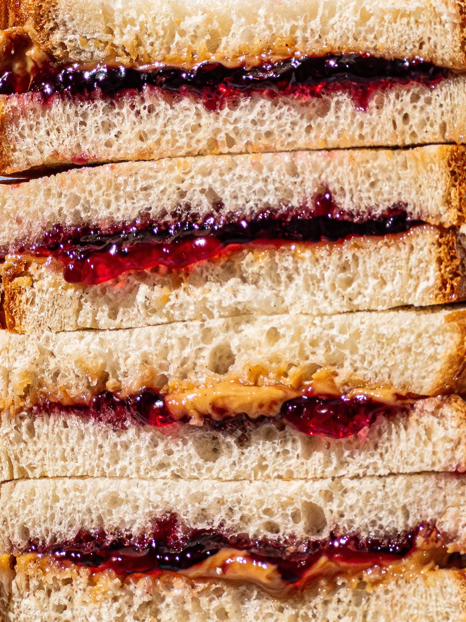 Close-up of stacked slices of bread with jelly and peanut butter spread inside.
