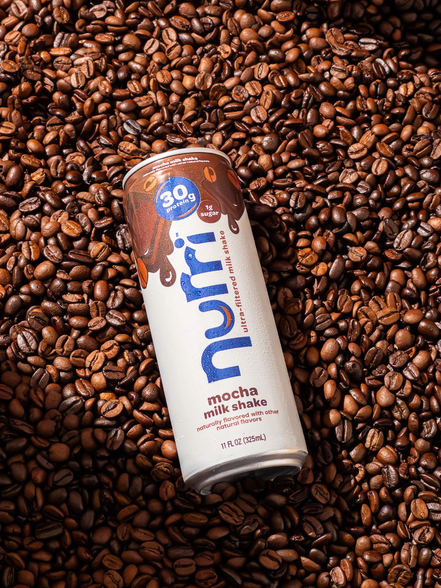 A can of Nutr by Mocha Milk Shake resting on roasted coffee beans.