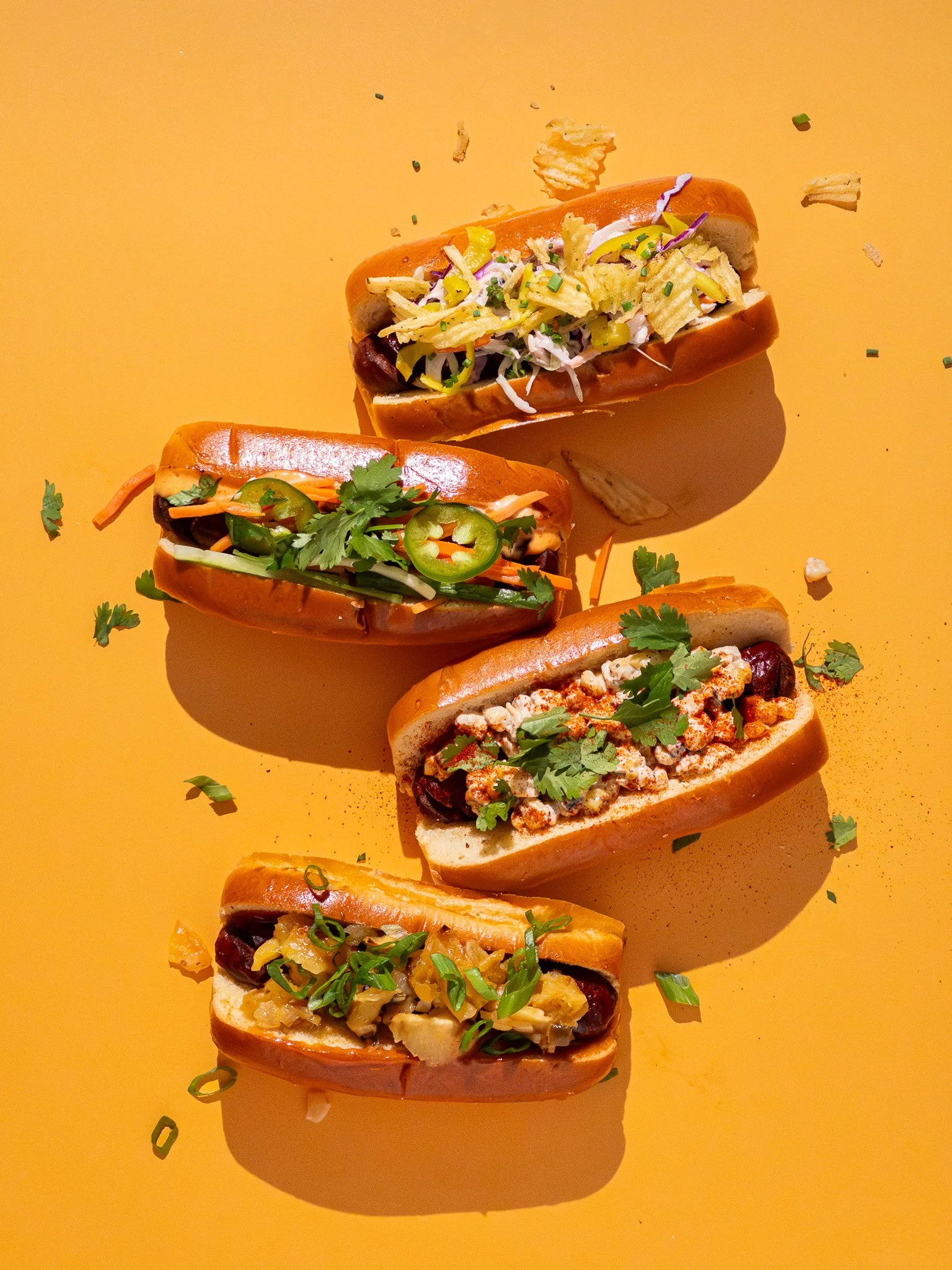 Five bao buns filled with various ingredients topped with chopped green onions and cilantro, spread on an orange surface.