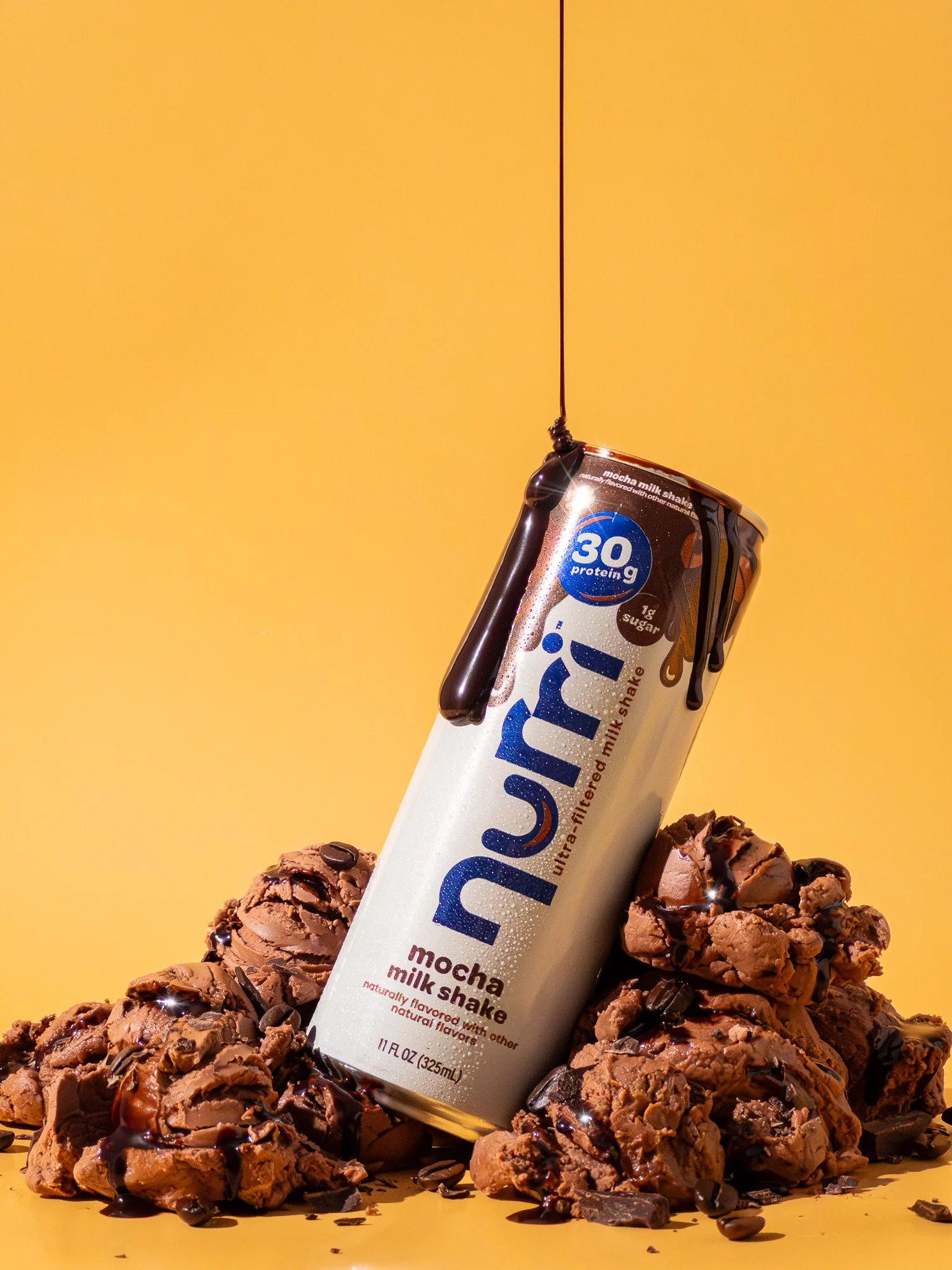 A can of Nuun Mocha Milk Shake flavored electrolyte drink positioned at an angle on a pile of chocolate chip cookie dough with chocolate syrup drizzled over them, set against a yellow background.
