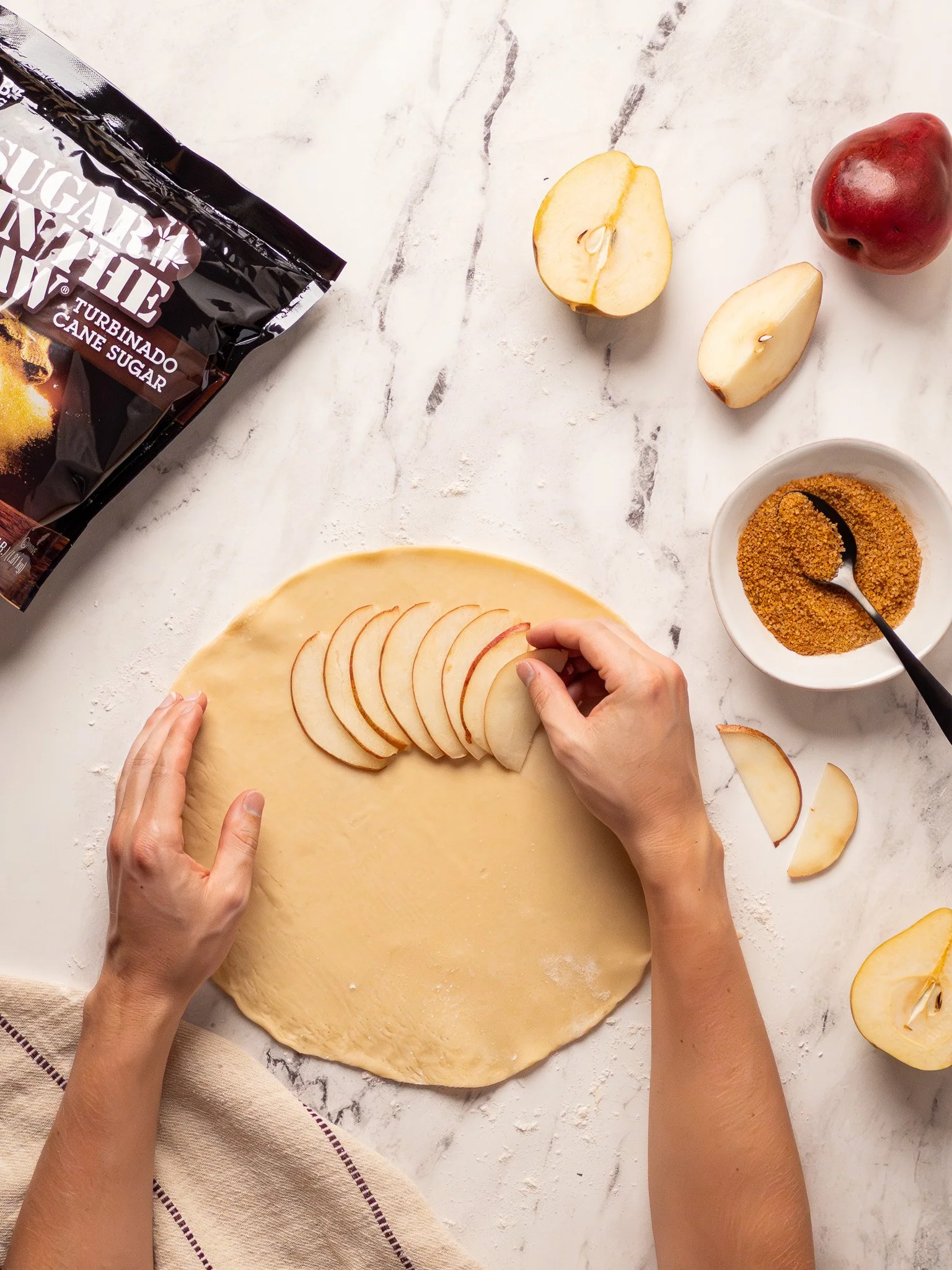 Preparing apple pastry dough with sliced apples, canned pie filling, and ingredients on a white marble surface.