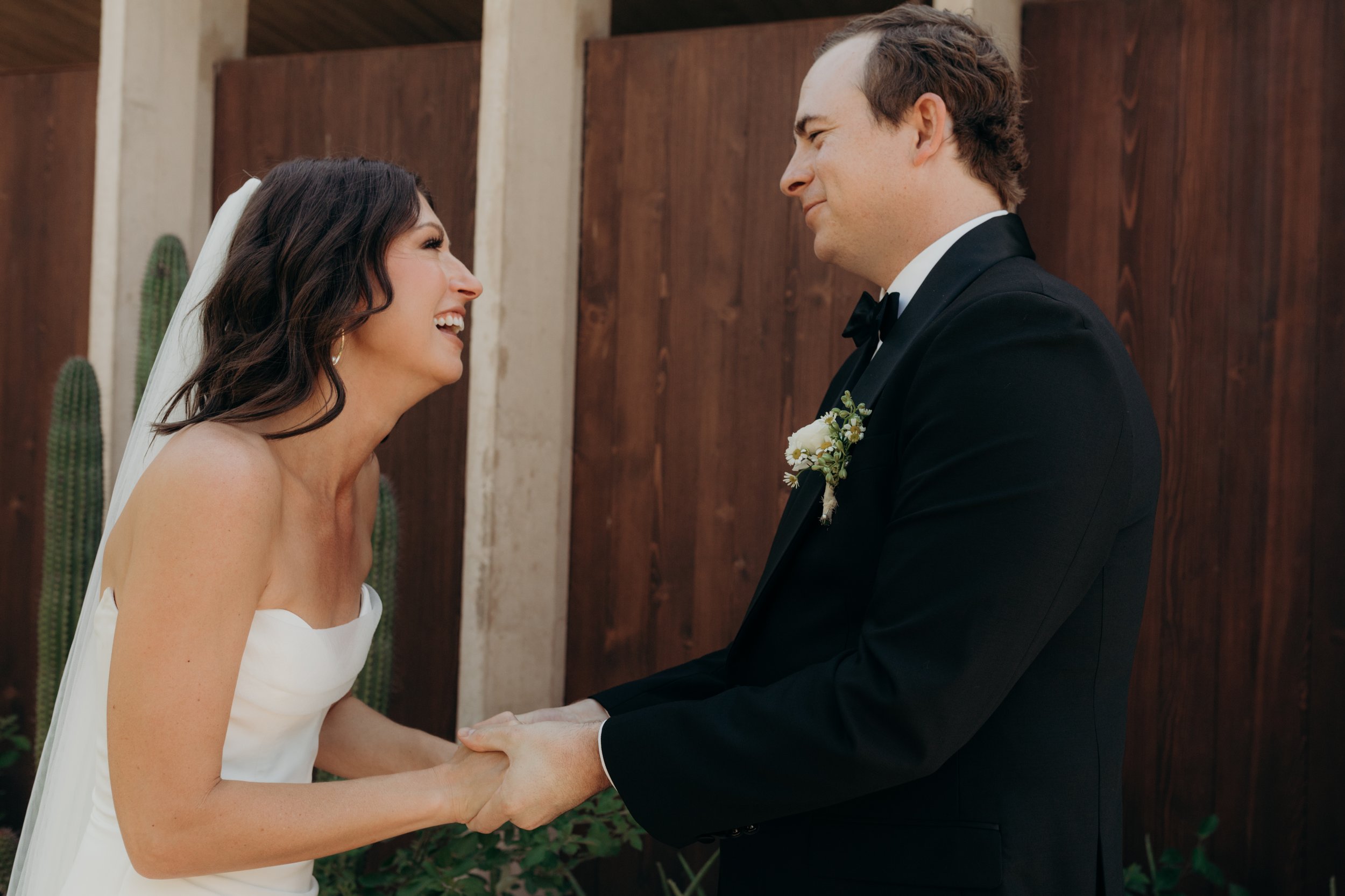 A bride and groom holding hands and smiling at each other during a wedding ceremony outdoors.