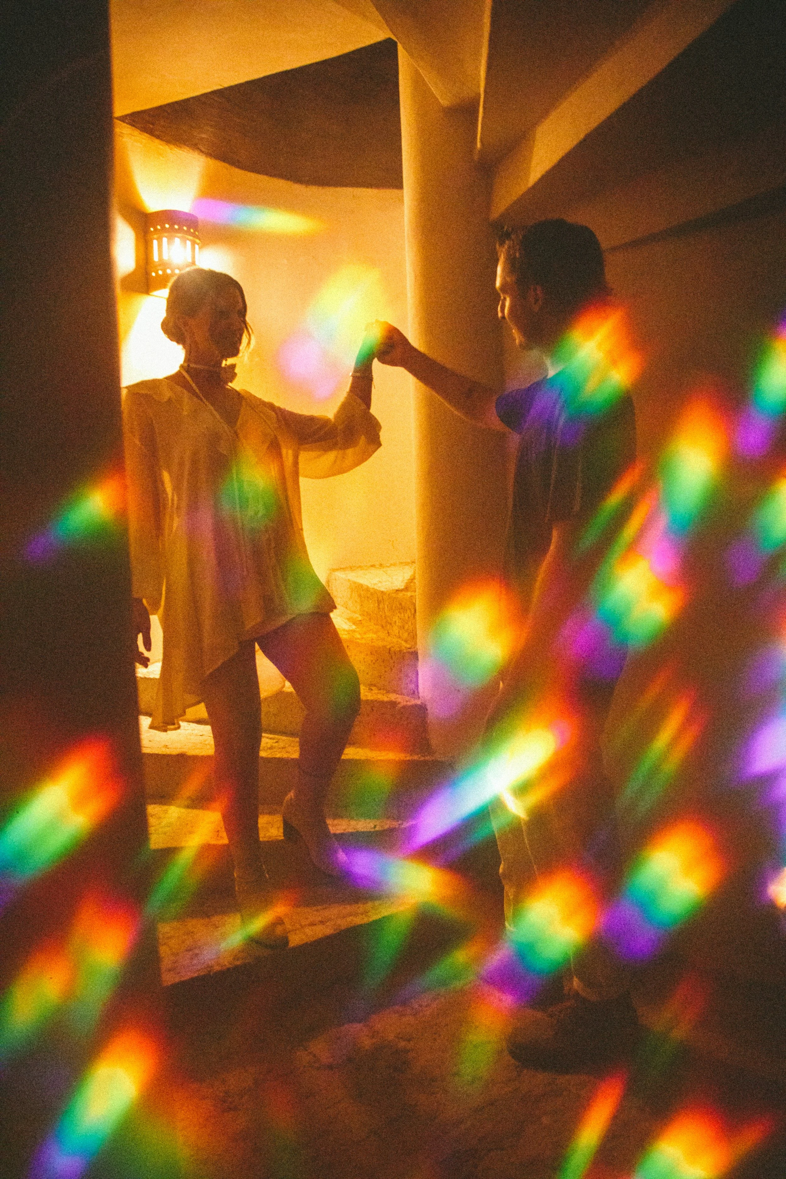A couple dancing in a warmly lit indoor space, with colorful light reflections creating a vibrant atmosphere.