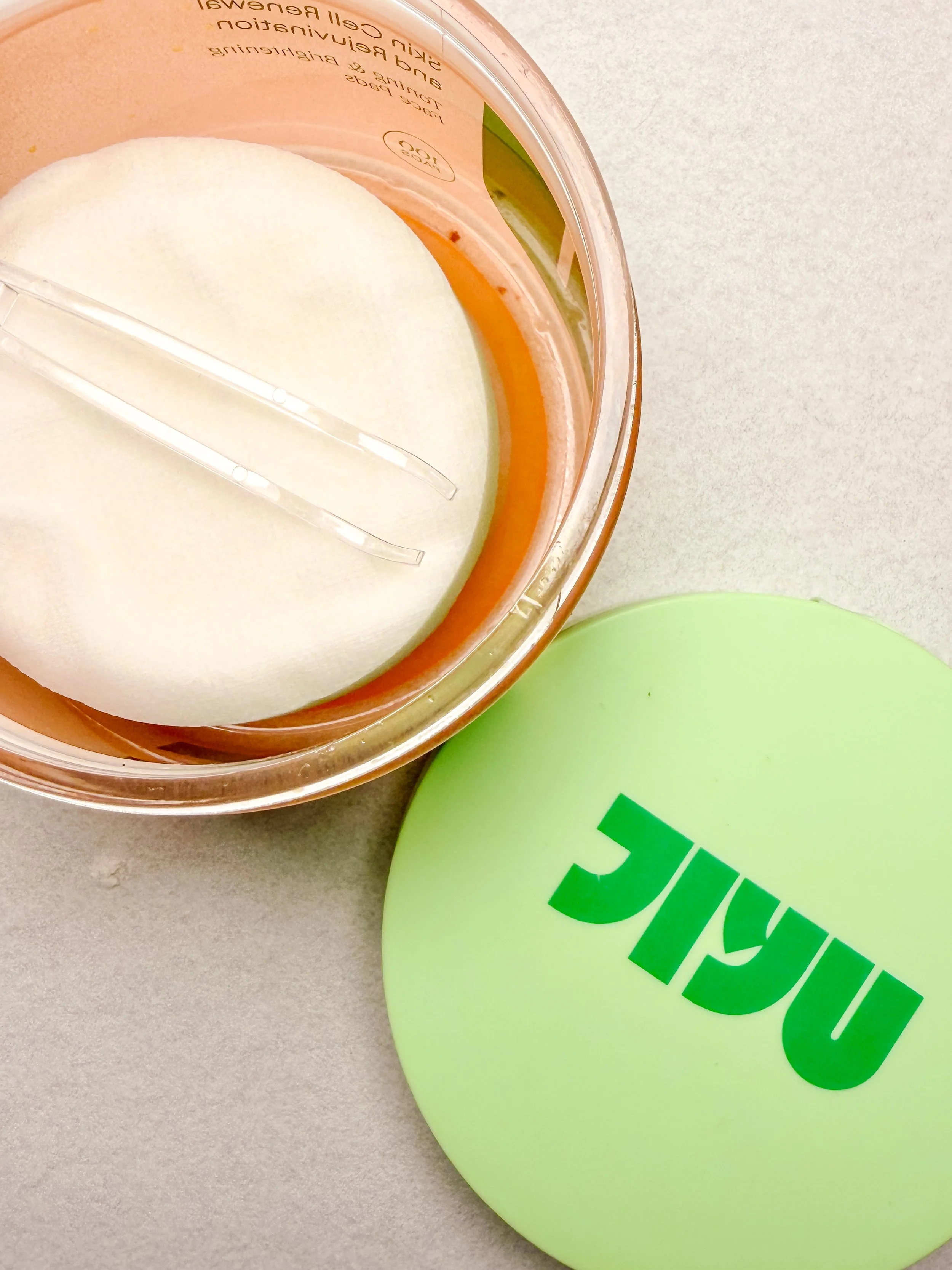 Part of a container of skin gel concealment and a green cylindrical object with the word 'VIVAL' in bold green letters.