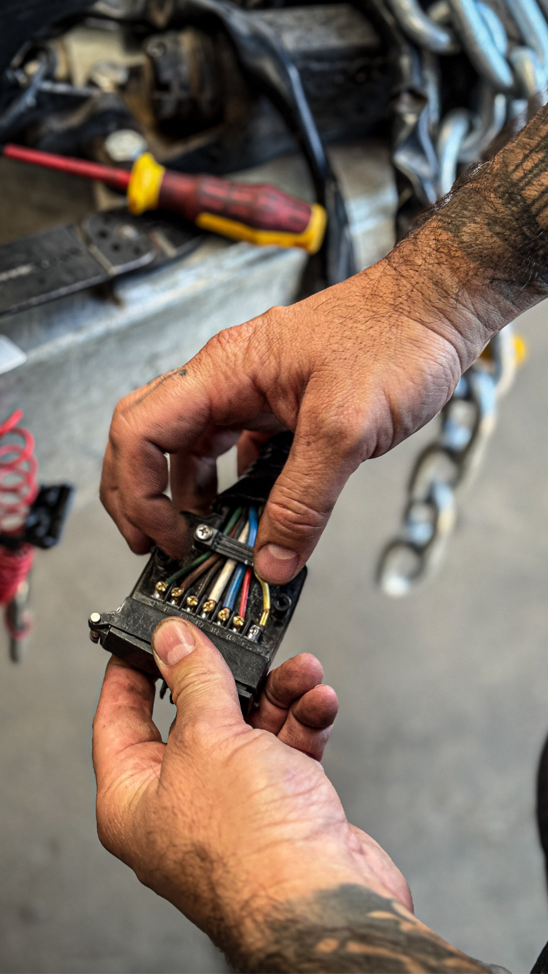 A person holding and inspecting an electrical wiring connector with multiple colored wires in a workshop or garage setting.