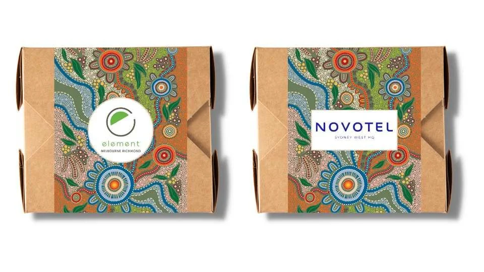 Two cardboard boxes with colorful Aboriginal-inspired patterns, one labeled "Element Melbourne Richmond" and the other "Novotel Sydney West HQ."