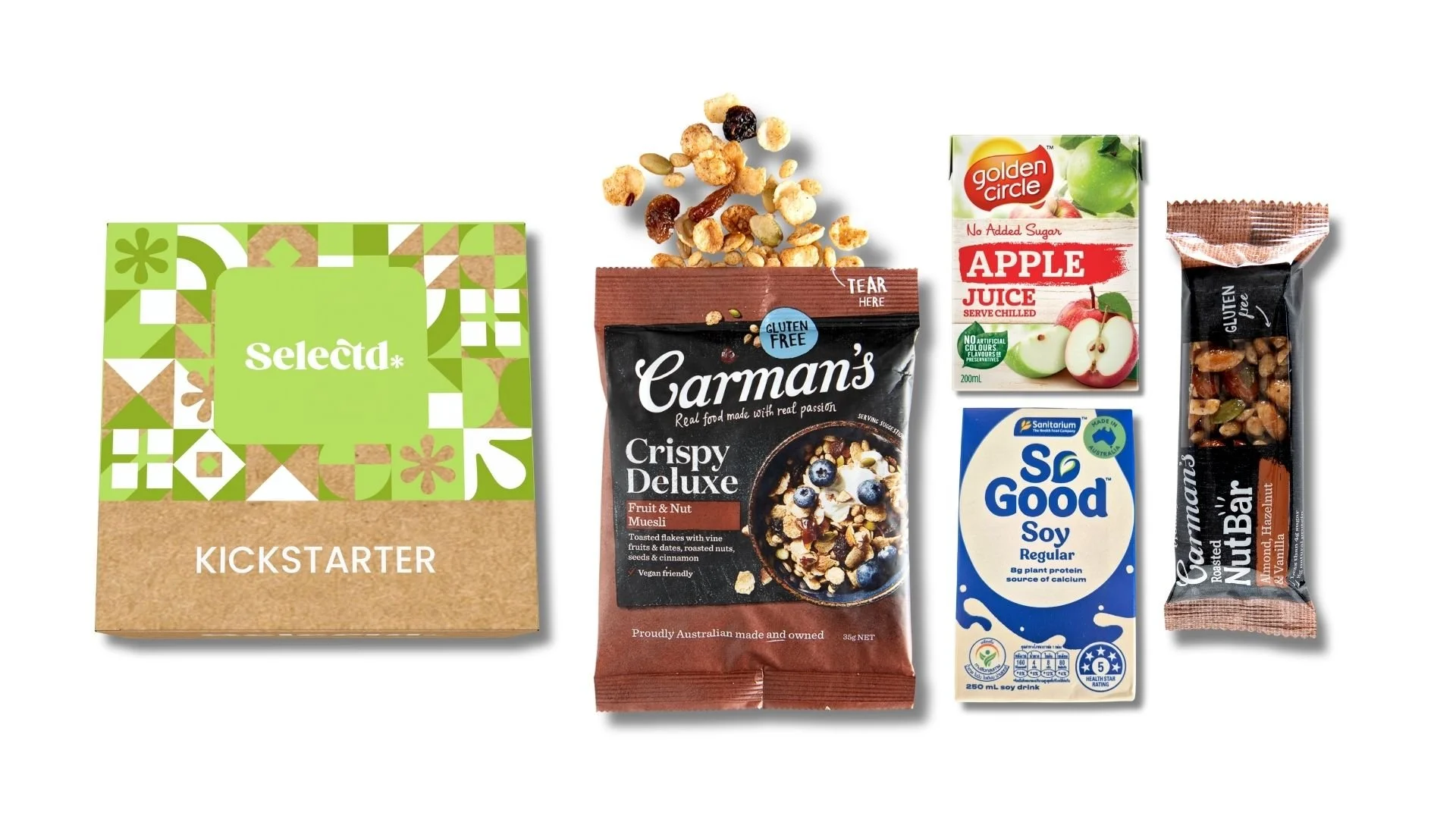 Assorted food items including a green and tan box of Selecta kickstarter, a bag of Carman's crispy deluxe fruit and nut muesli, a small carton of Golden Circle apple juice, a soy milk carton, and a nut bar, with some muesli spilling from the bag.