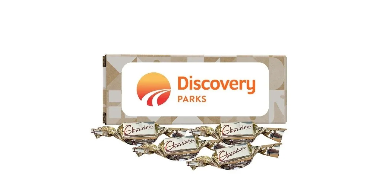A pack of four chocolates with "Chocolatier" written on the wrappers, placed below a Tiny Treat customised box with the Discovery Parks logo on it.