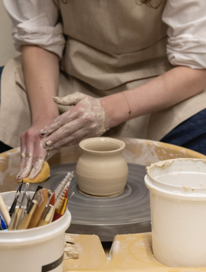Persona trabajando en cerámica en un torno de alfarero, usando herramientas de modelado.