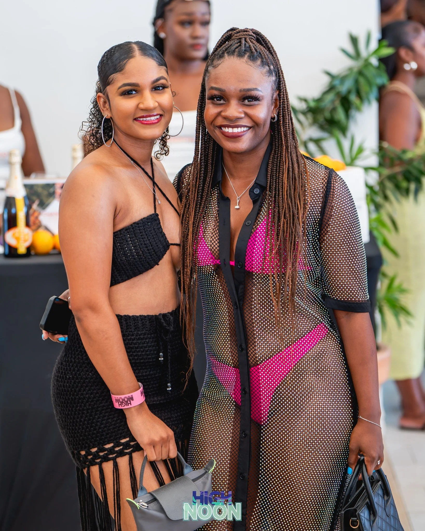 Two women standing together at an indoor event, dressed in swimwear and casual stylish outfits, smiling at the camera.