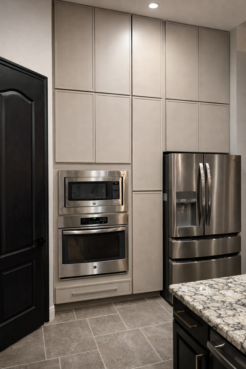 Modern kitchen with stainless steel refrigerator, microwave, and oven, beige cabinetry, and a granite countertop.