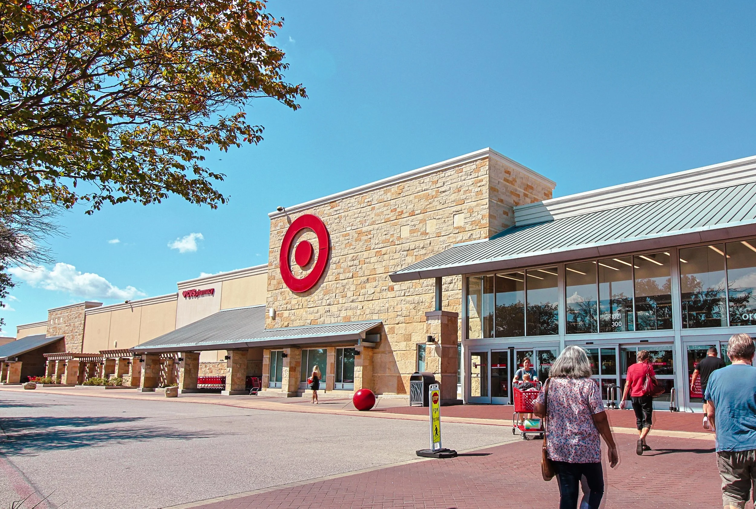 Exterior view of a Target store at Wolf Ranch Town Center in Georgetown, TX, with a large red target logo on the brick wall, people walking towards the entrance on a sunny day with a clear blue sky.