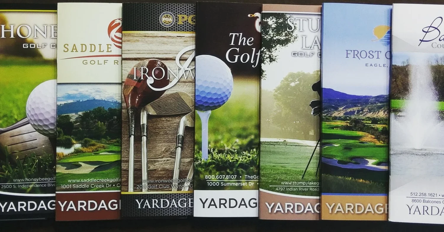 A row of printed yardage guides produced for individual golf courses