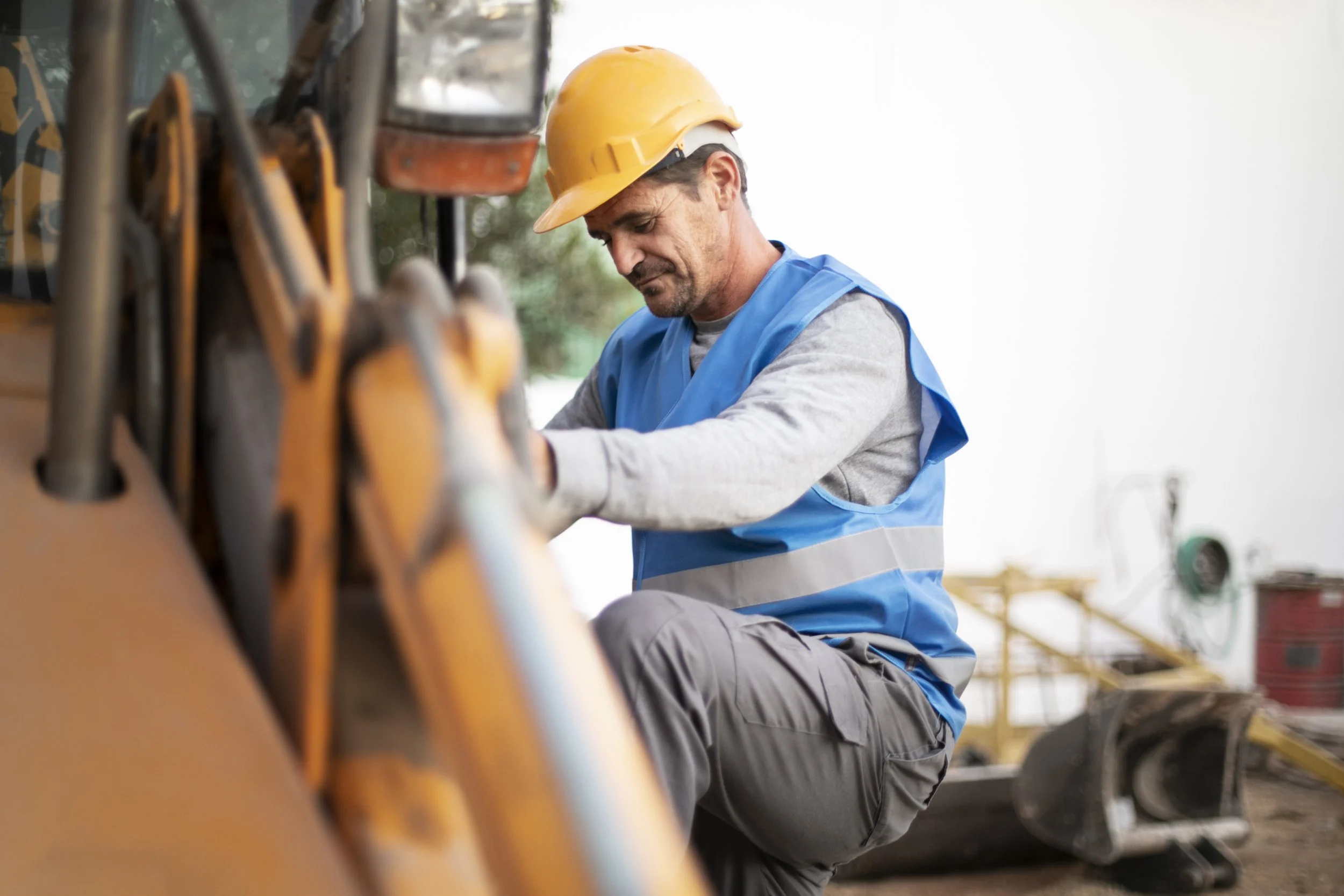 A construction worker wearing a yellow helmet and a blue safety vest working on heavy machinery outdoors.