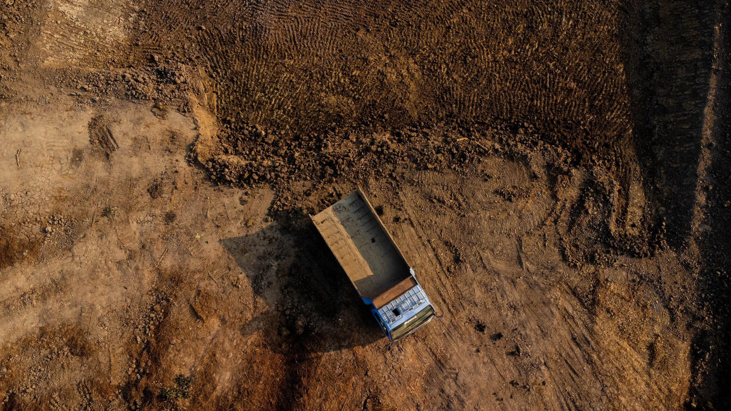 An aerial view of a construction site with a dump truck on uneven dirt ground.