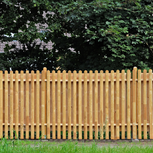A wooden privacy fence with vertical slats, set on a grassy area, with trees and foliage in the background.