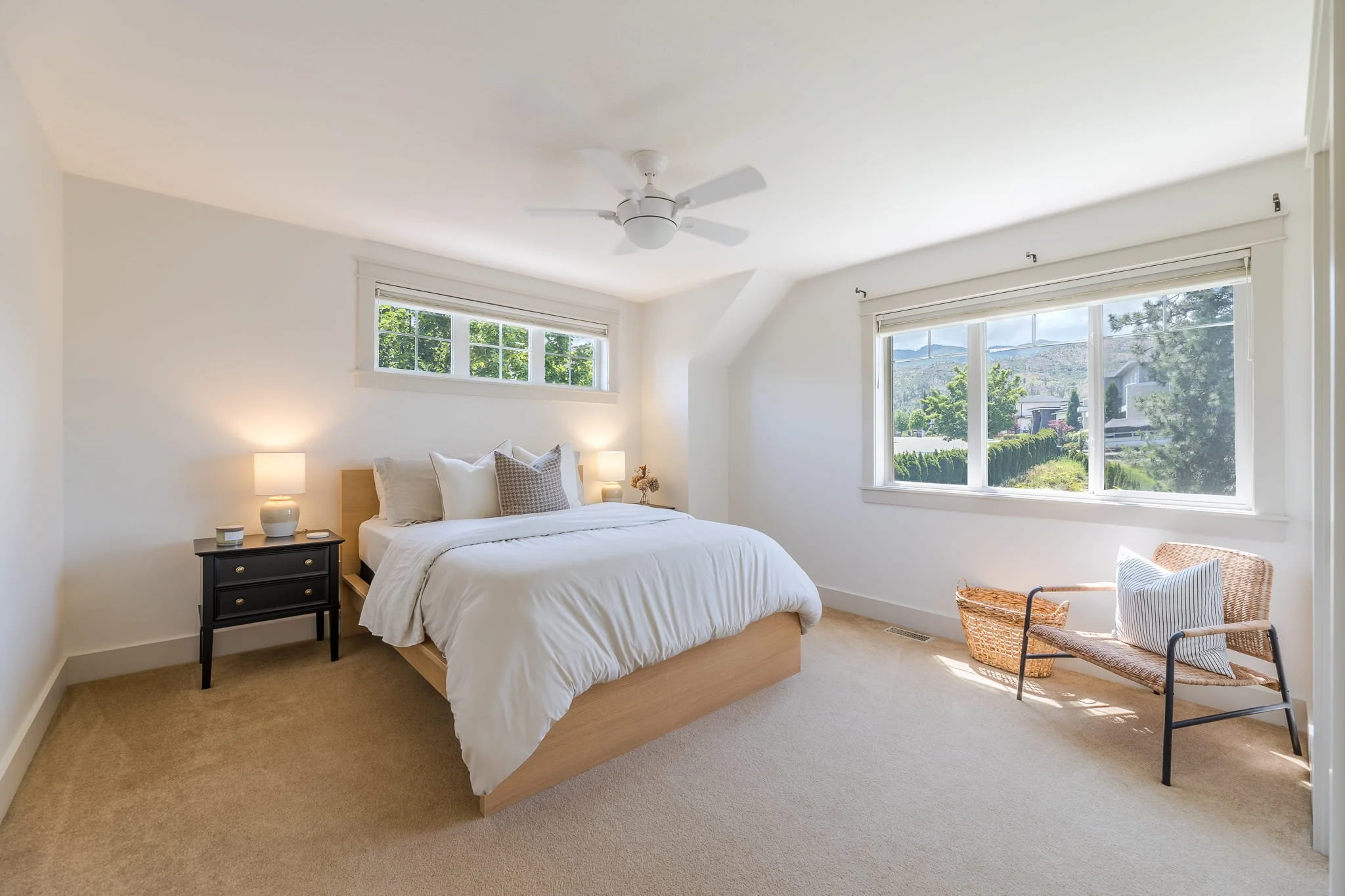 Bright bedroom with a bed, nightstand with lamps, a chair, window with a view of trees and mountains.