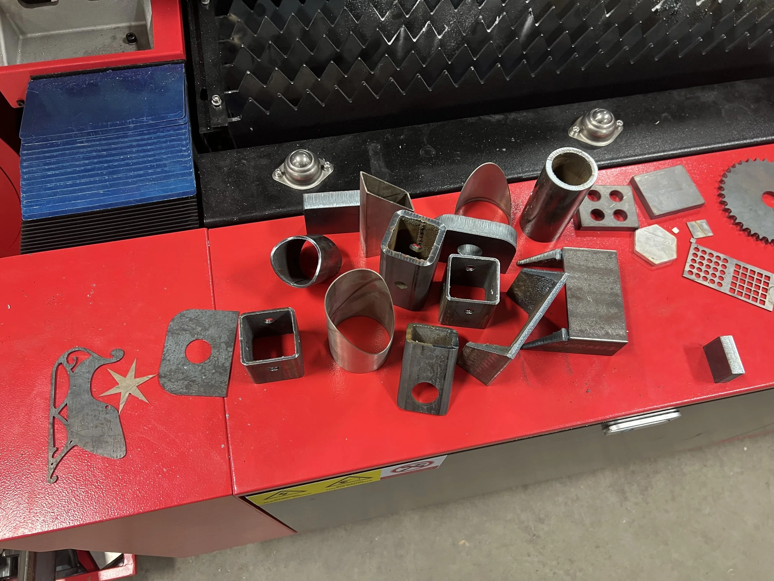 Various metal pieces and parts on a red work table, with some plastic and metal sheets nearby.