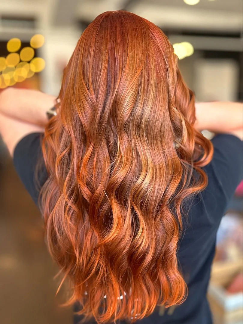 Back view of a woman with long, wavy, reddish-brown hair.