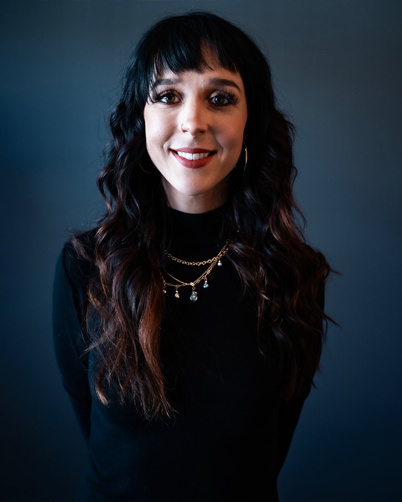 Hannah Smothers (Dyedarlin) standing against a dark background, smiling at the camera.