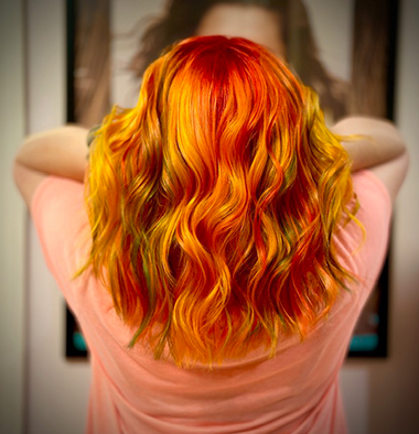 Person with vibrant, wavy orange and yellow hair looking at a mirror.