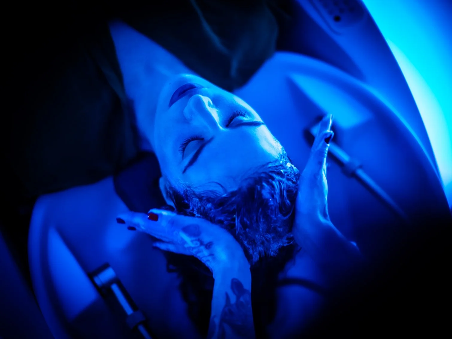 A person with eyes closed, illuminated by blue light, receiving Japanese Head Spa treatment.