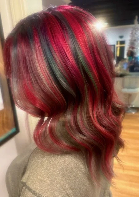 Side view of a woman with shoulder-length, wavy hair dyed in vibrant shades of red, pink, black, and hints of green.