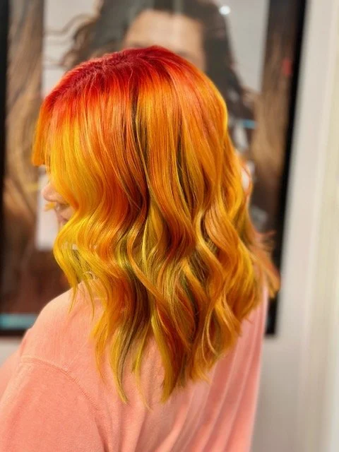 Woman with long, wavy hair dyed in red, orange, and yellow gradient shades.