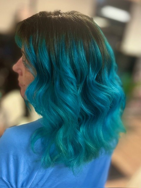 Side view of a woman with wavy, shoulder-length hair that fades from dark at the roots to bright blue at the tips.
