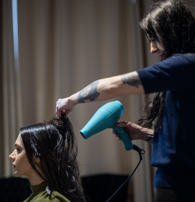 Hannah Smothers (Dyedarlin) blow-drying another woman's hair salon, with a curtain in the background.