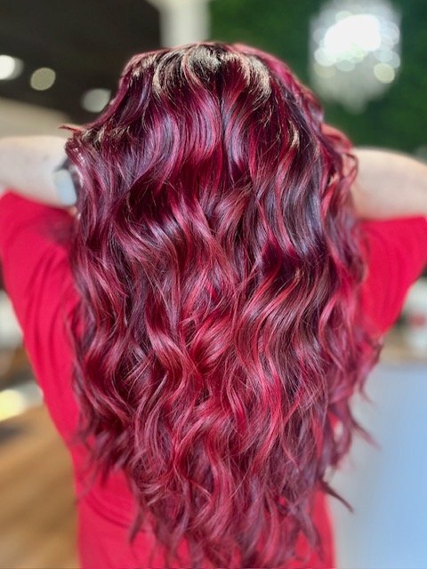 Back view of a person with long, curly, vibrant red hair wearing a red shirt.