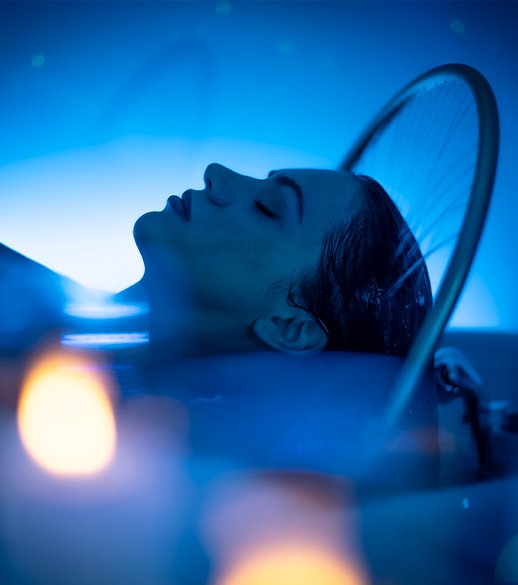 A woman lying down in Japanese Head Spa with a calm expression, surrounded by blue lighting and candles.