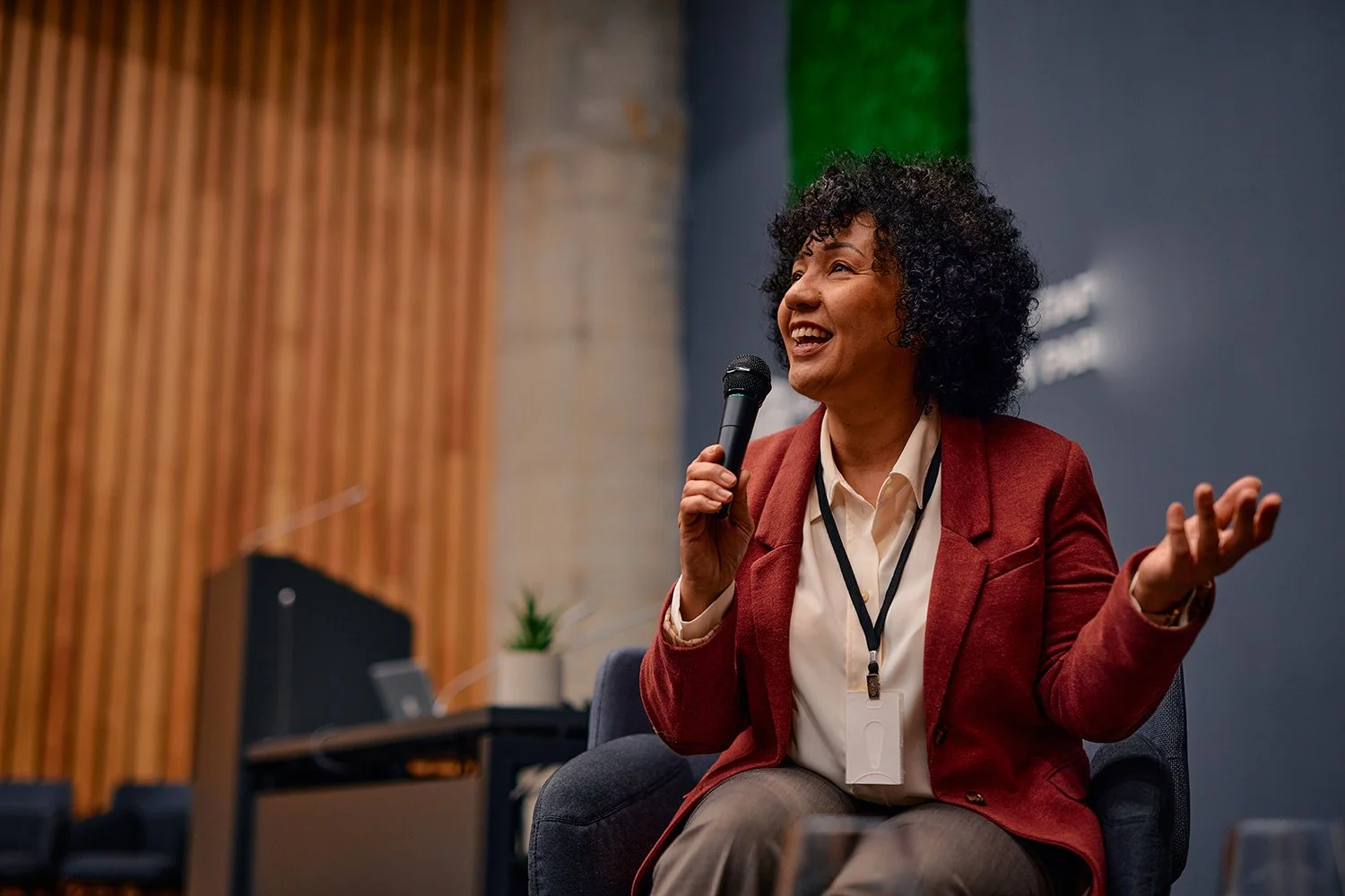 Woman in an orange blazer speaking into a microphone.