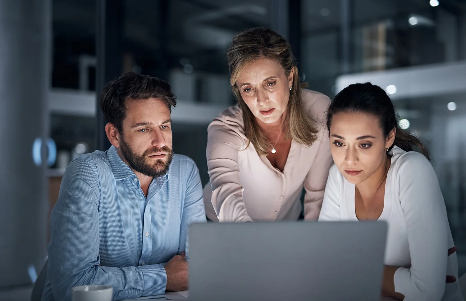 Three people looking concerned while viewing a computer screen.