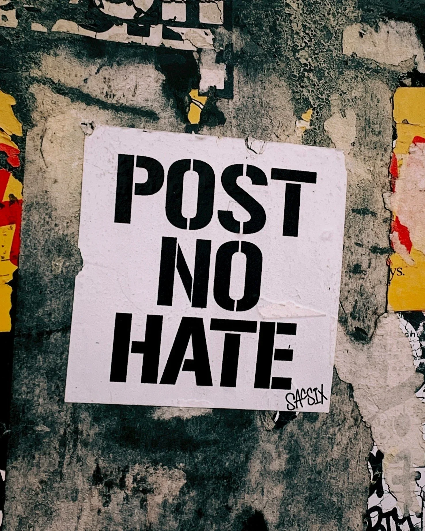 A poster on a graffitied wall reads 'Post no hate'