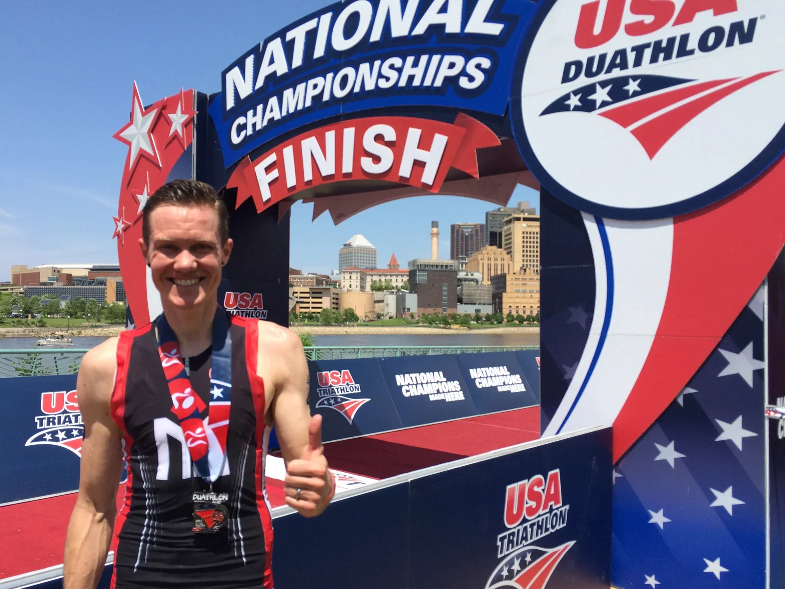 Chris Mosier smiles and gives the thumbs-up sign at the finish of the USA Duathlon