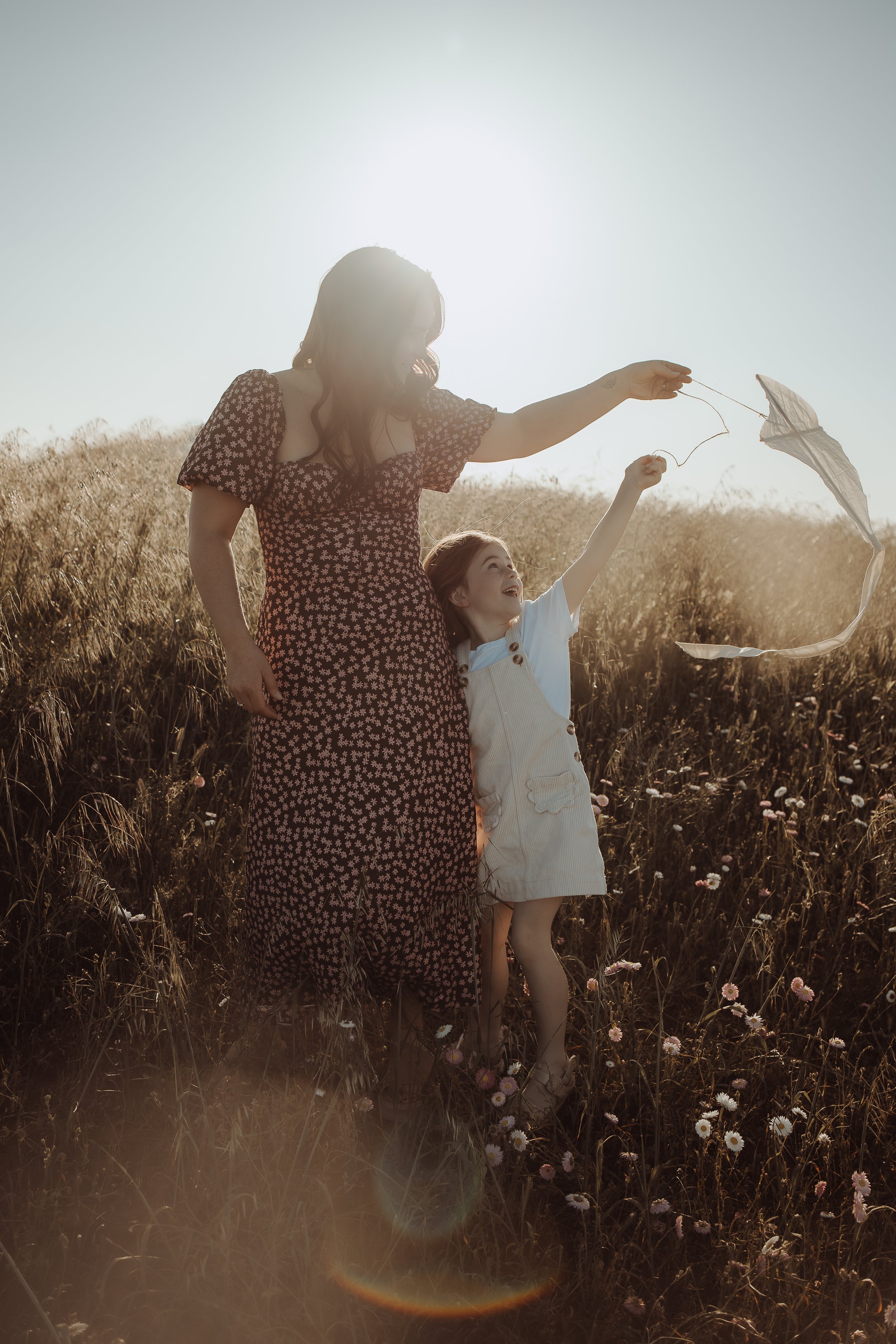 A woman and a young girl outside in a field flying a kite during sunset.