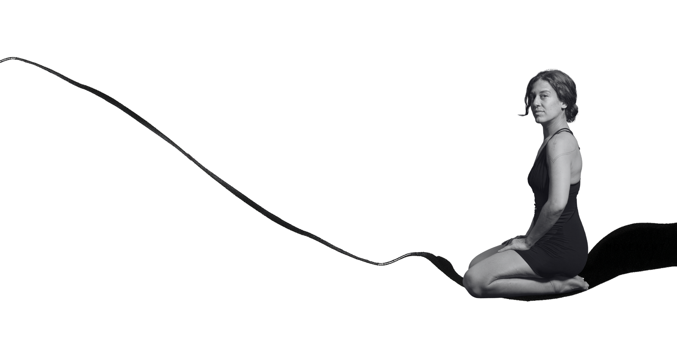 A woman sitting on a large, abstract, black and white shape resembling a paintbrush stroke, with her body slightly angled to the right, wearing a sleeveless black dress, and looking towards the camera.