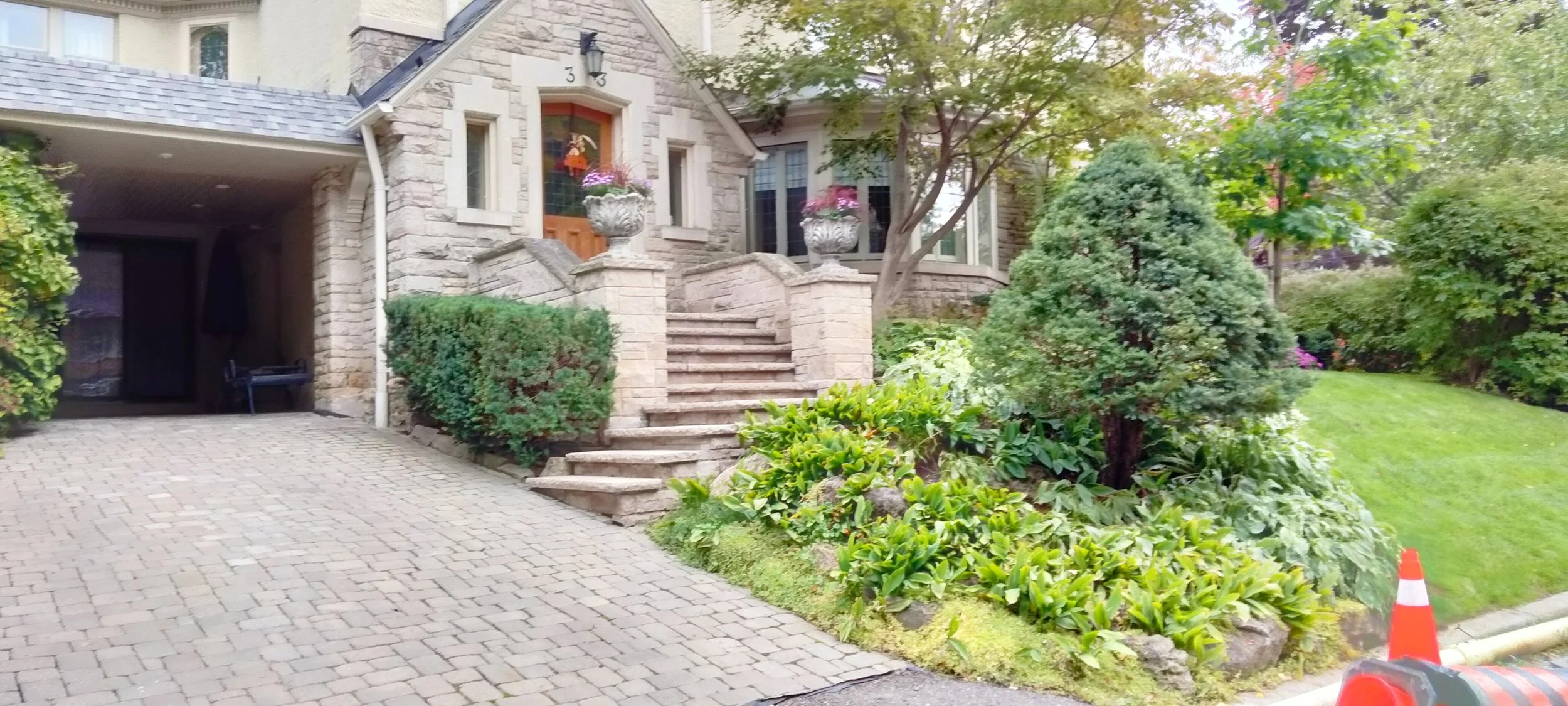 Stone house entrance with stairs, potted flowers, bushes, and trees in the garden.