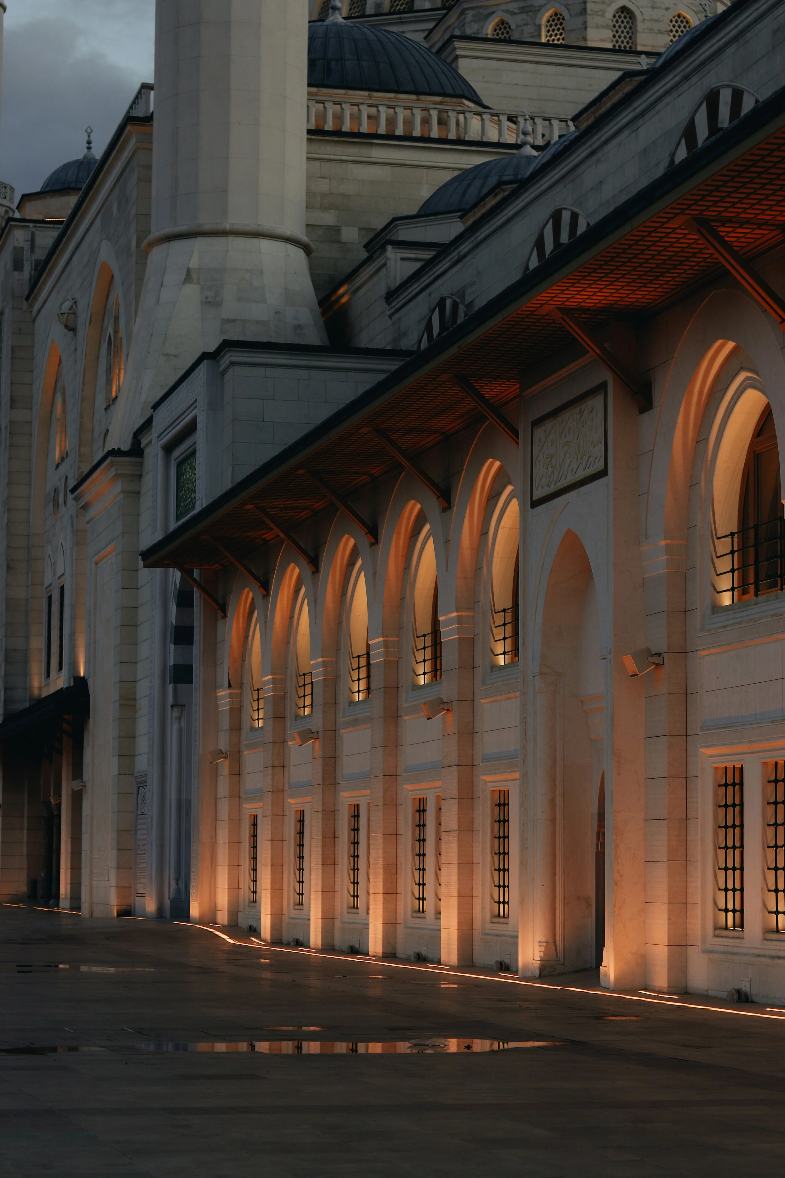 Nighttime view of an ornate building with arched windows and warm lighting, featuring domes and minarets, resembling Islamic architecture.