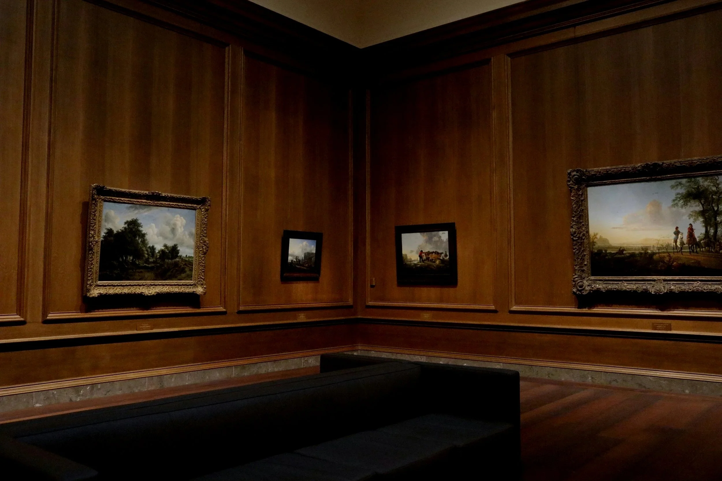 Interior of an art gallery with four landscape paintings on wooden walls.