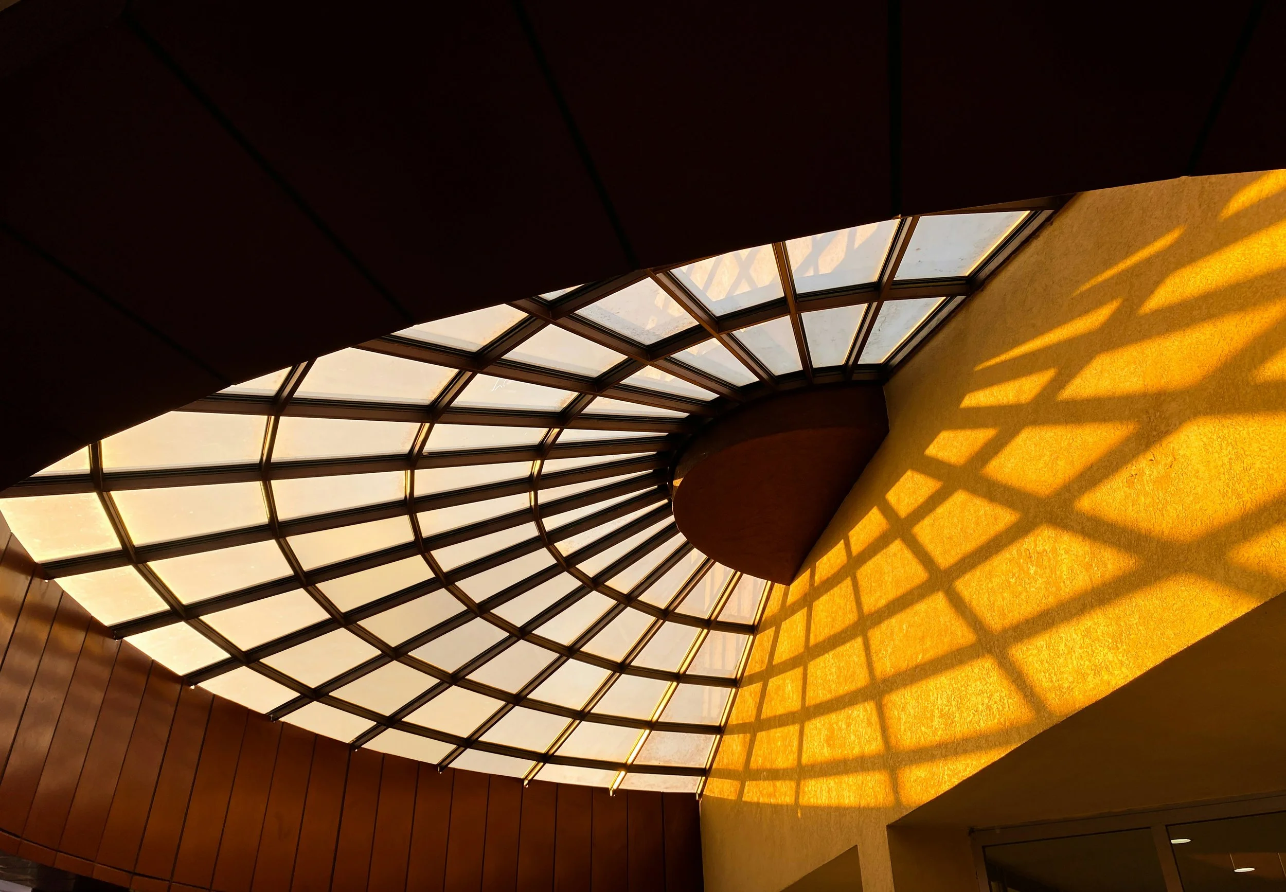Interior view of a glass dome ceiling casting shadows on yellow walls.