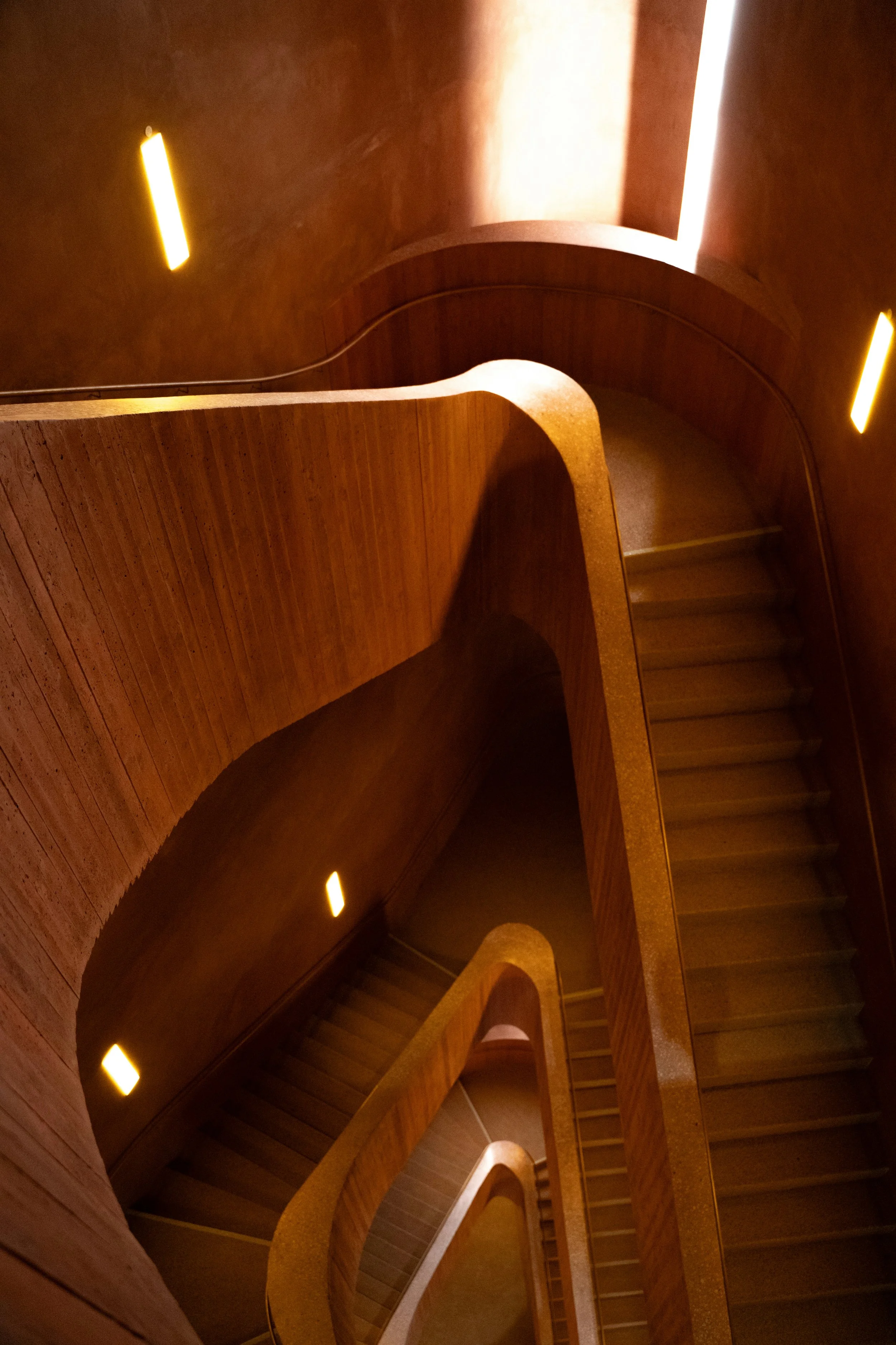 Multi-level indoor staircase with wooden railings and warm lighting.