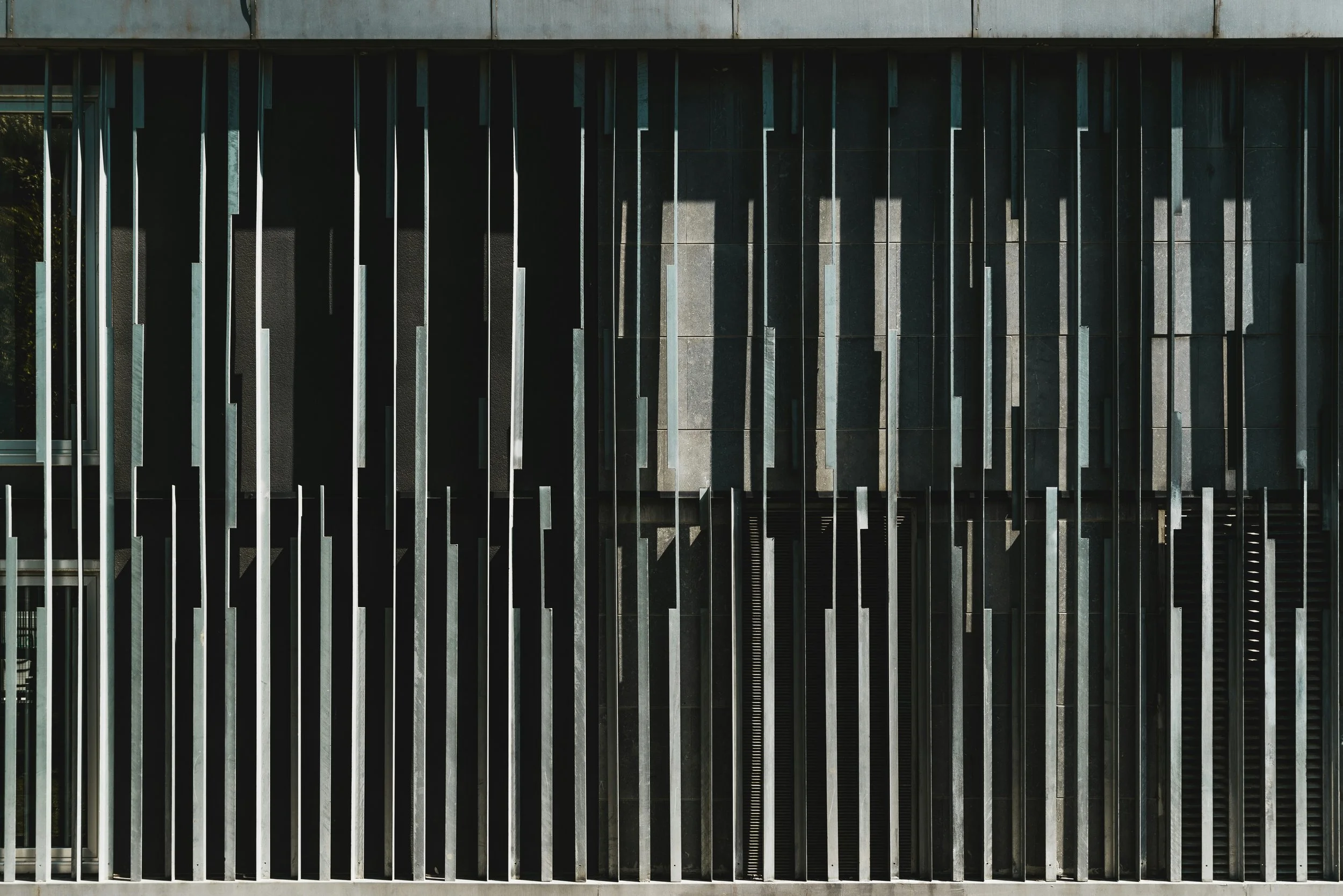 Close-up view of a modern building facade with vertical black metal bars and gray stone wall panels