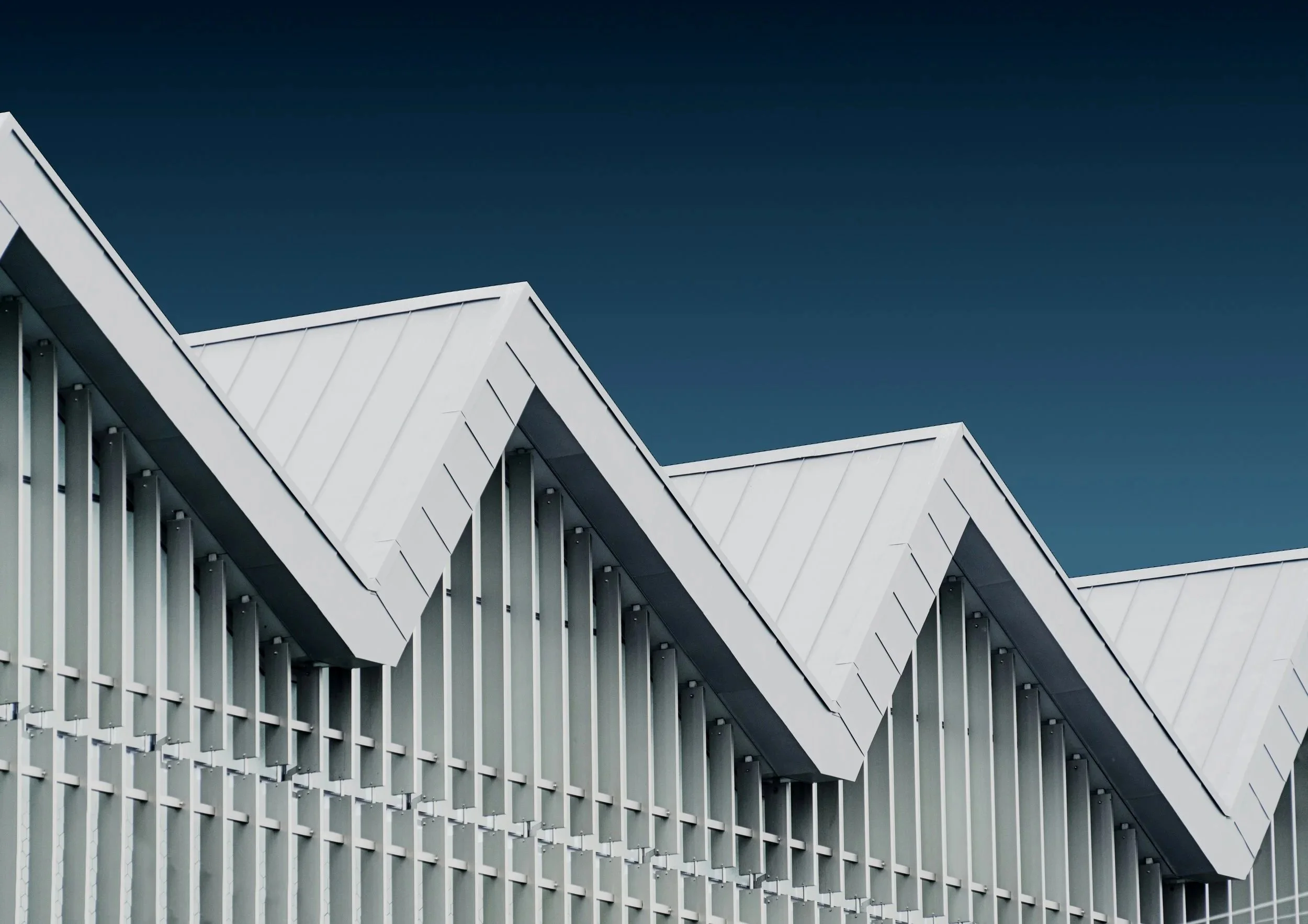 Modern building with geometric white roof structures and vertical slats, against a dark blue sky.