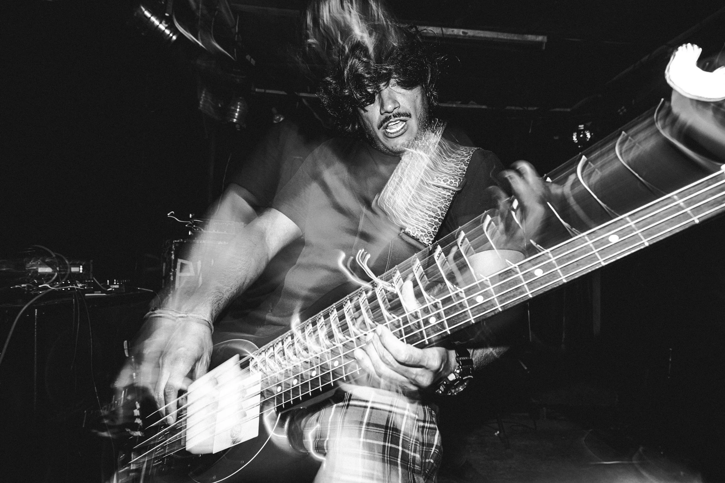 A man with curly hair playing an electric guitar on stage, with motion blur and smoke effects, in a black and white photo.