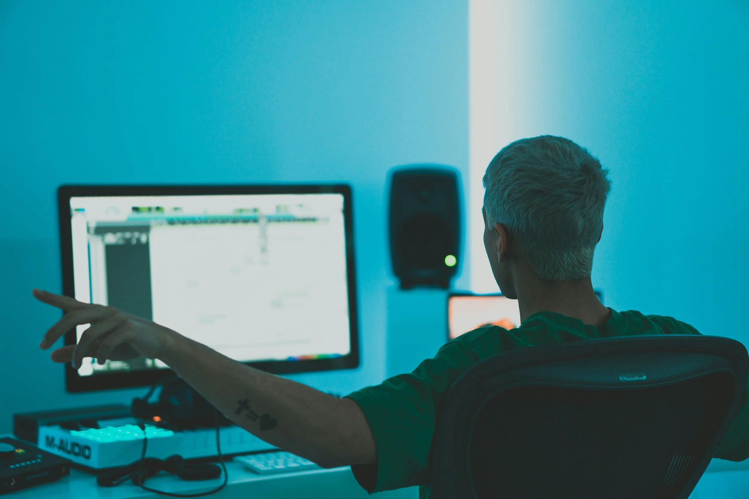 Person with gray hair working on a computer in a dimly lit room, with a blue hue, facing away from the camera.
