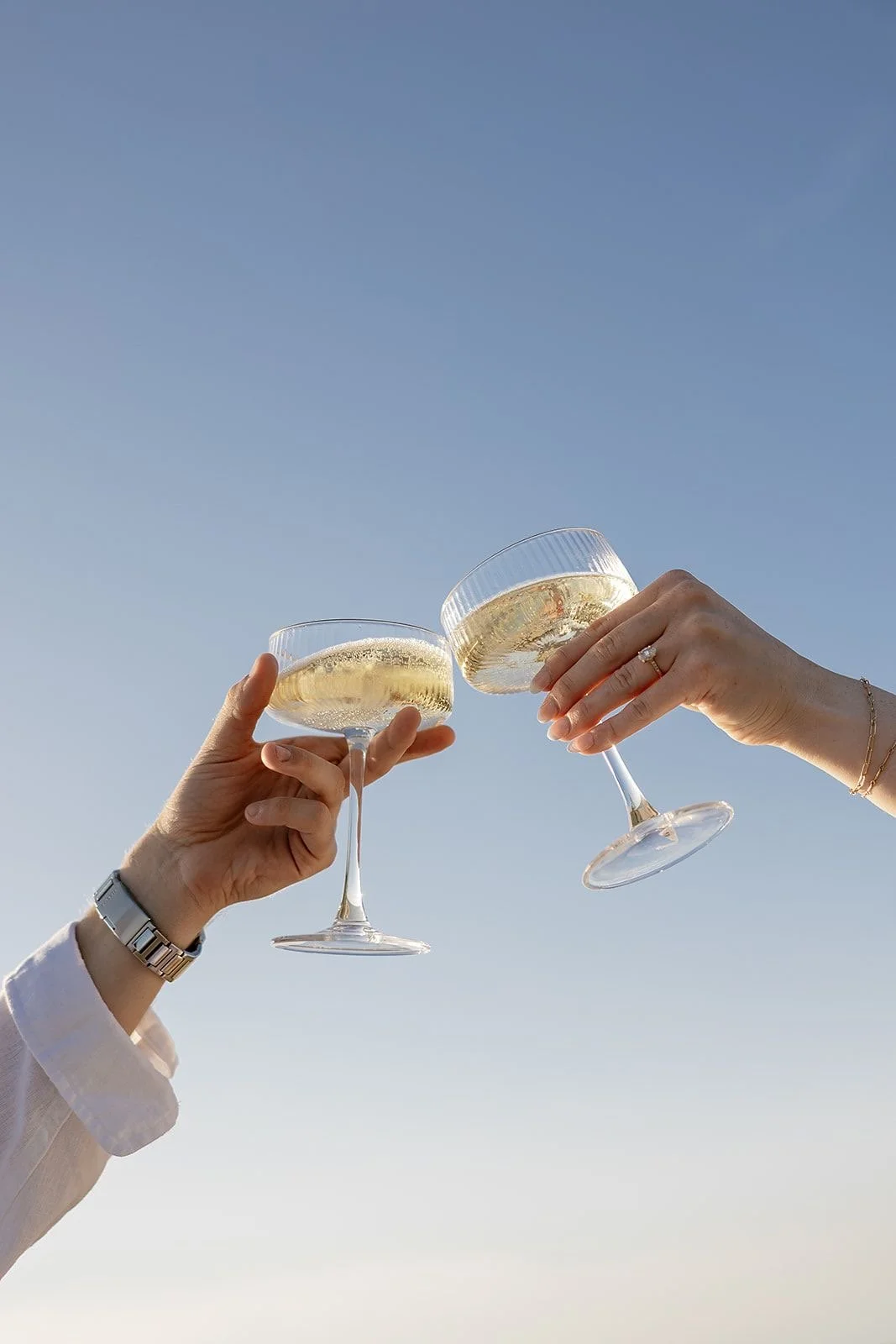Two people clinking glasses of champagne against a clear blue sky.
